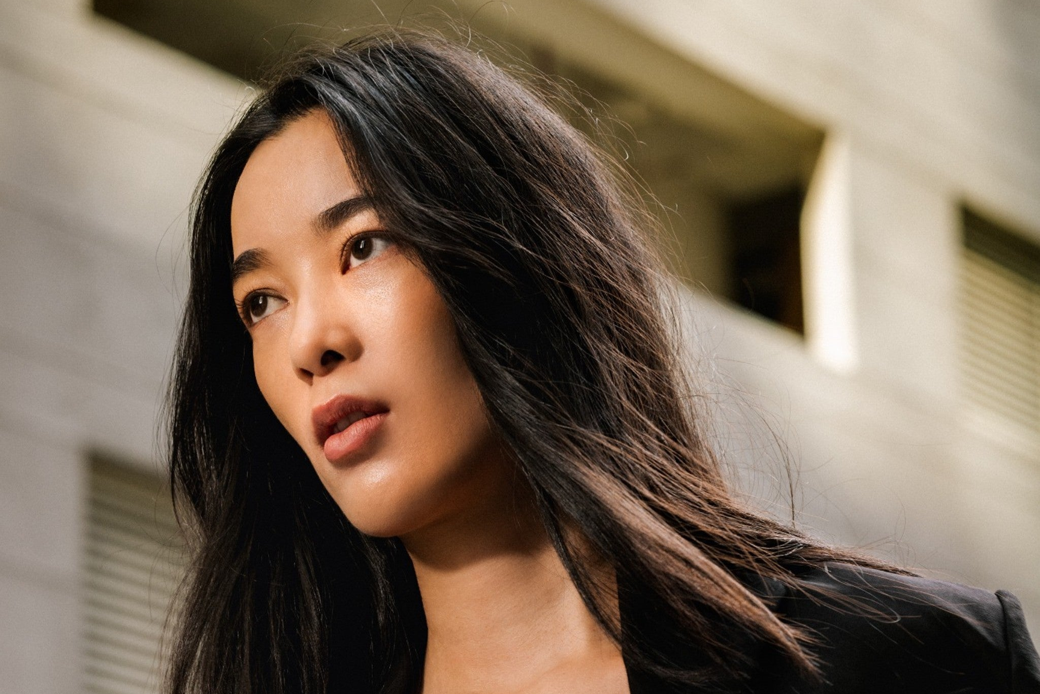 Woman wearing a black blazer over a white top against a blurred urban background